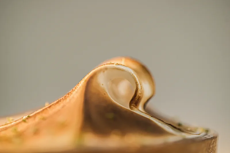 A slice of calamansi meringue tart lying on its side, showing the pale custard layer beneath torched meringue.