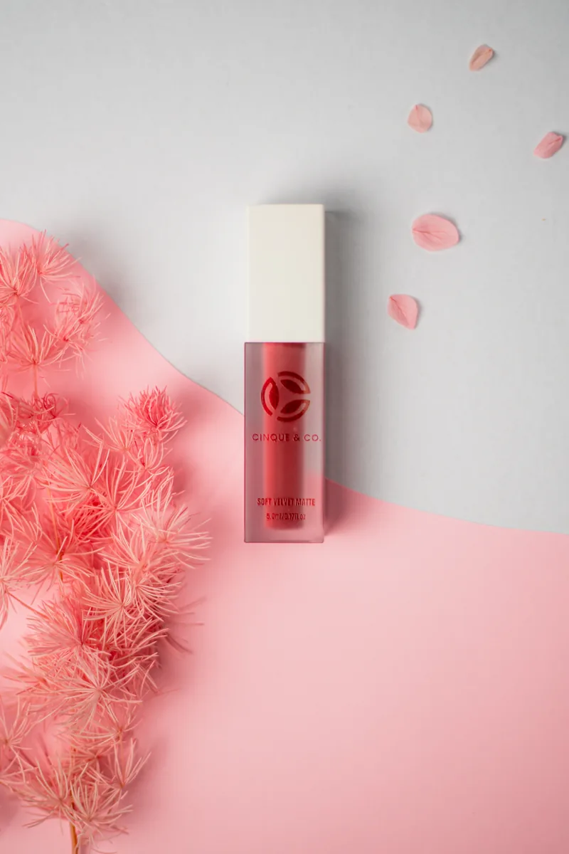A tint bottle on a pink ground beside feathery dried blooms.