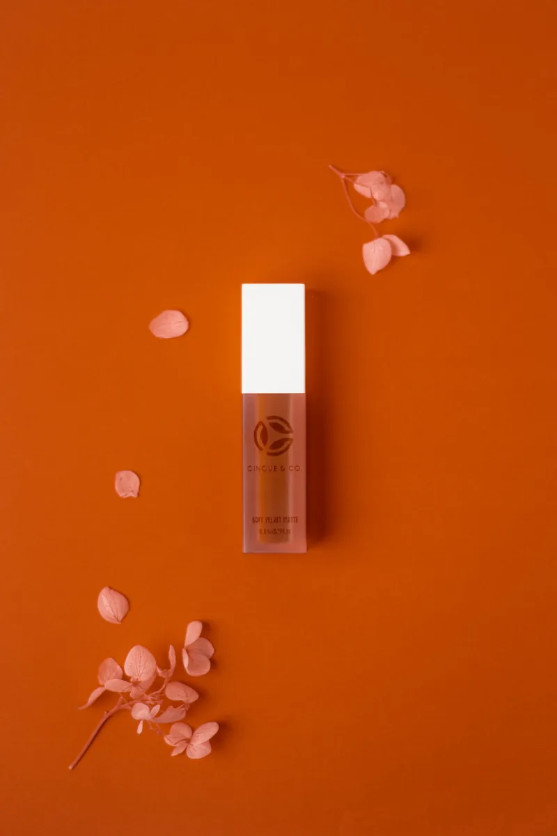 A single tint bottle laid on a rust orange ground with scattered petals.