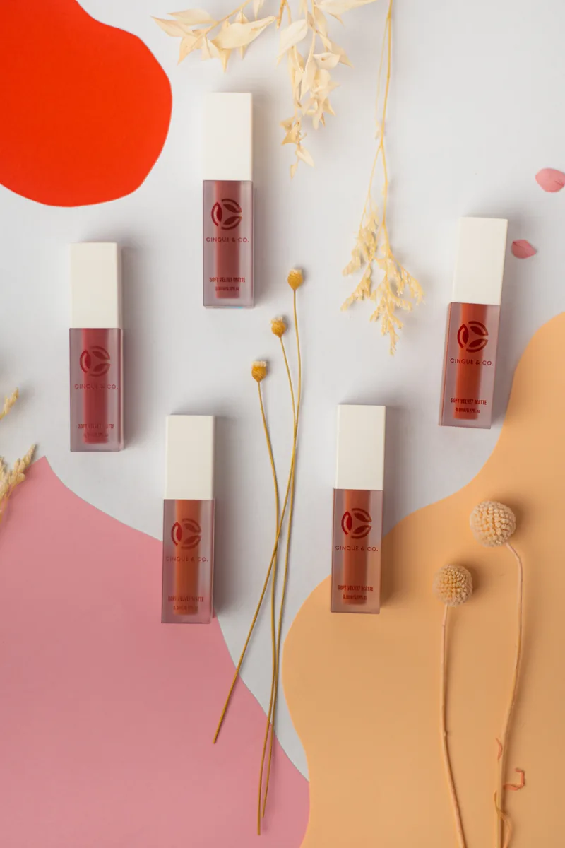 Six tint bottles scattered across orange and pink paper waves.
