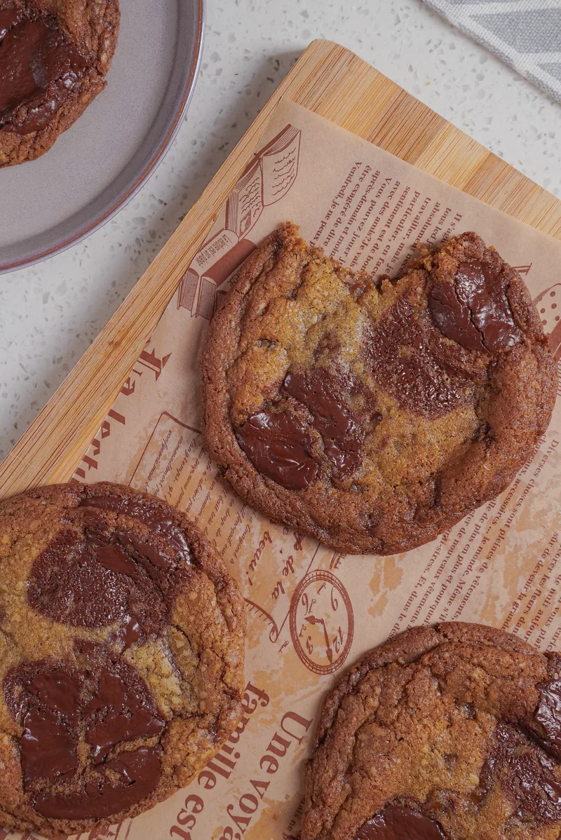 Overhead of thick chocolate chunk cookies on printed baking paper.
