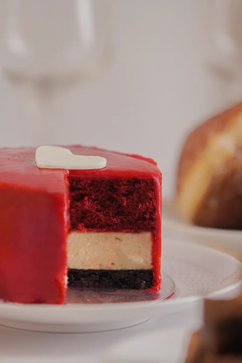 A heart topped red cake cut open to show red velvet and cheesecake layers.