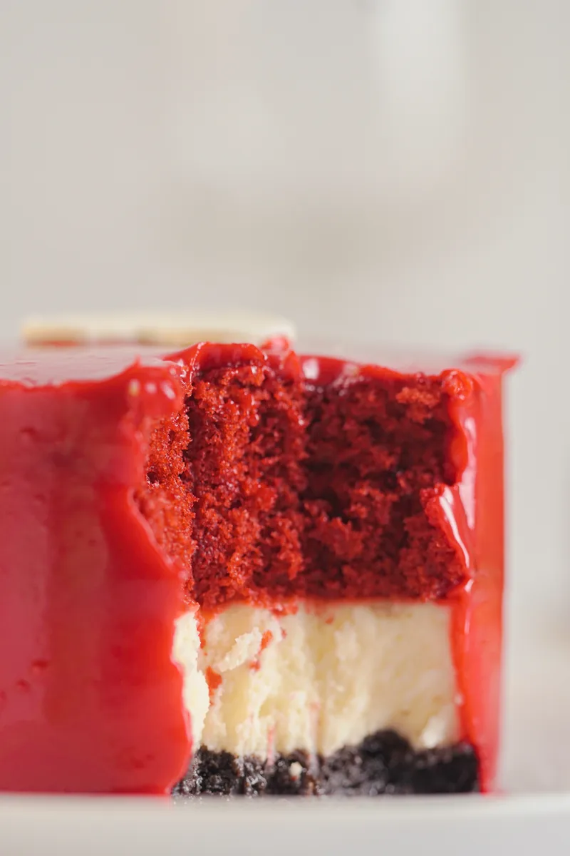 A macro cross section of red glaze, crumb and cheesecake.