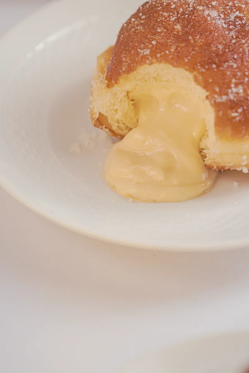 A sugared doughnut split with custard flowing onto the plate.