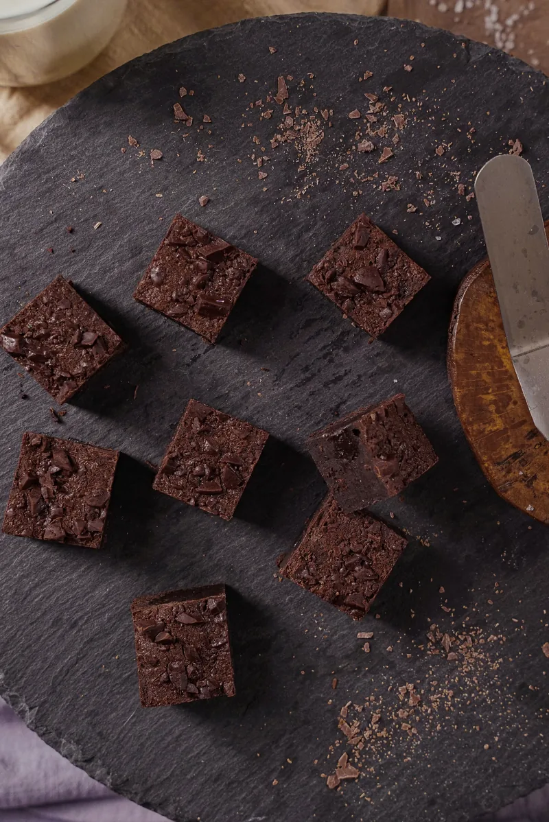 Brownie squares scattered across a dark slate round with a palette knife at the edge.
