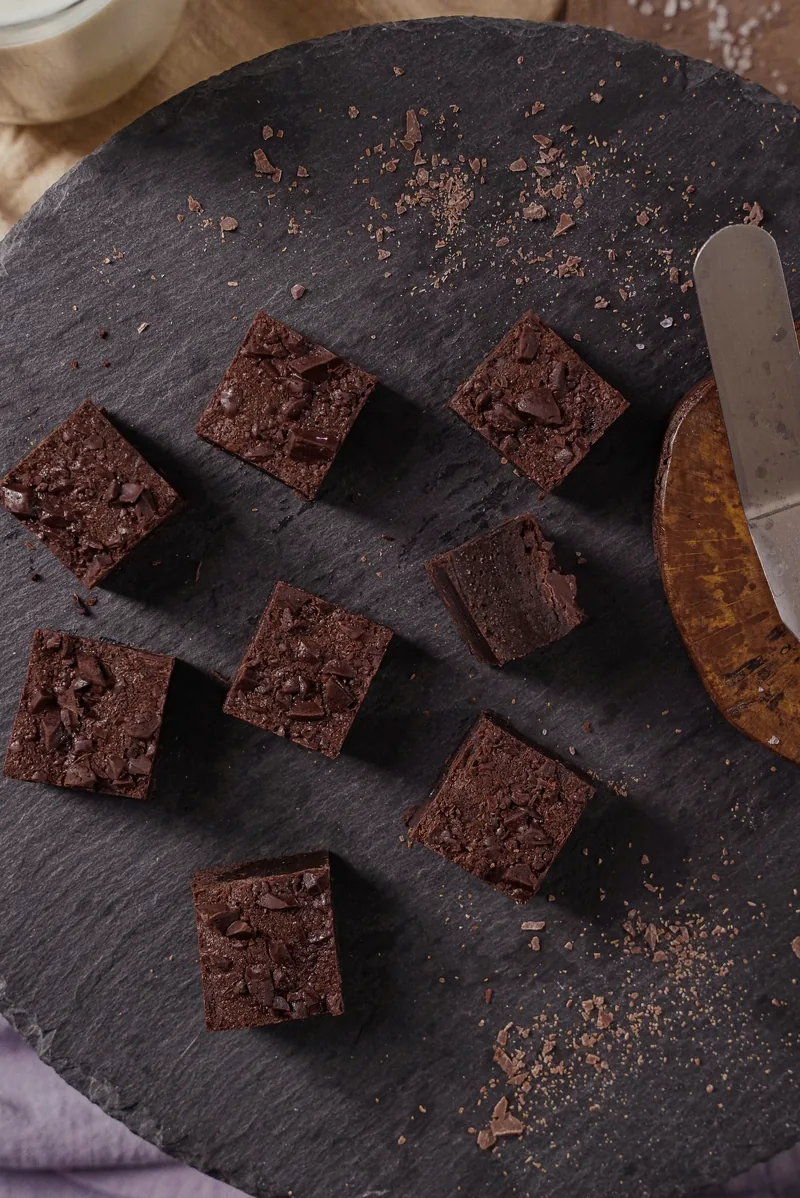 Brownie squares close on dark slate, crumbs and chocolate shards around them.