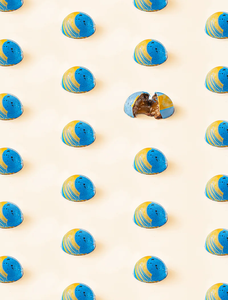 A repeating pattern of blue and yellow bonbons on cream, one broken open at the centre.