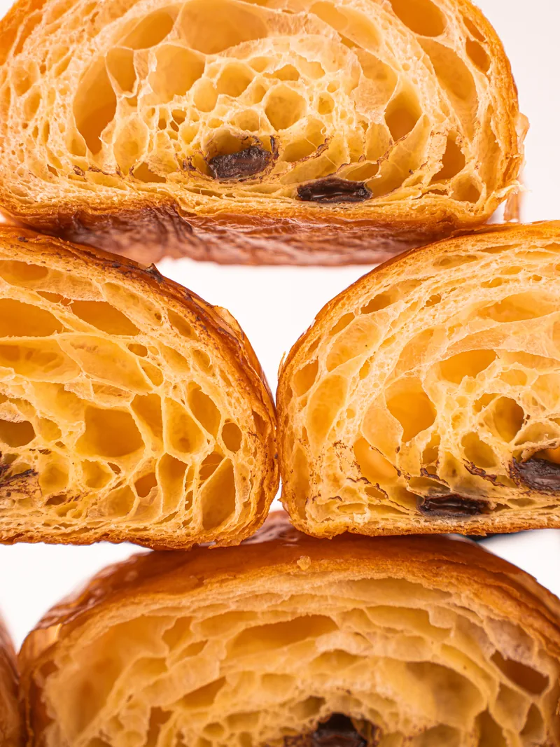 A close stack of viennoiserie cut open, the honeycomb crumb filling the frame.