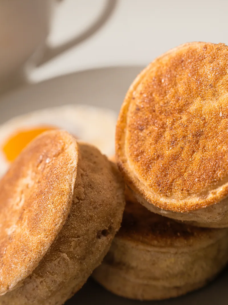 Split english muffins leaning against a coffee cup, browned tops forward.