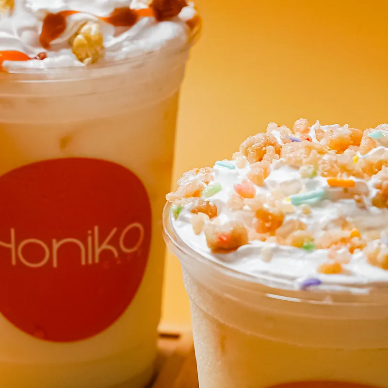 Close on whipped cream and candied toppings crowding two branded cups.