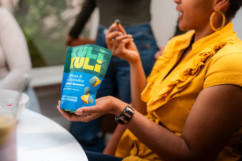 Two women mid laugh at a table set with Kuli Kuli products and drinks.