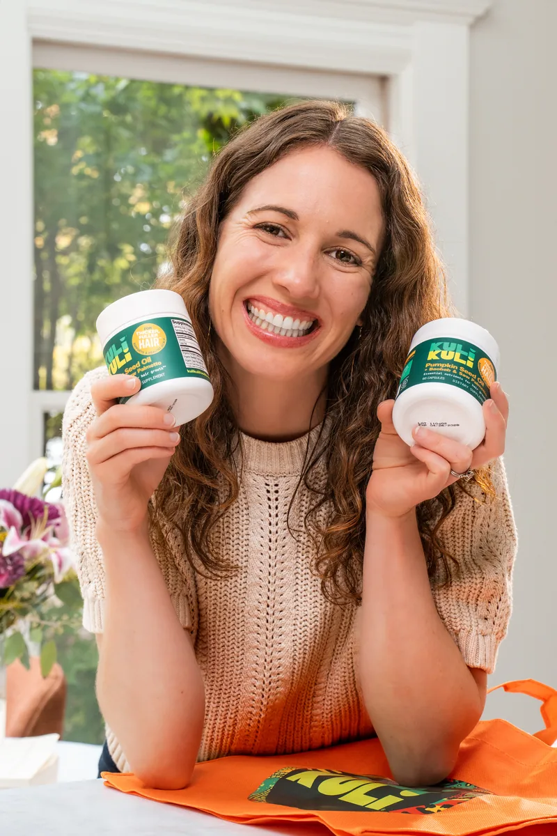 A woman holding two Kuli Kuli tubs up beside her smile.
