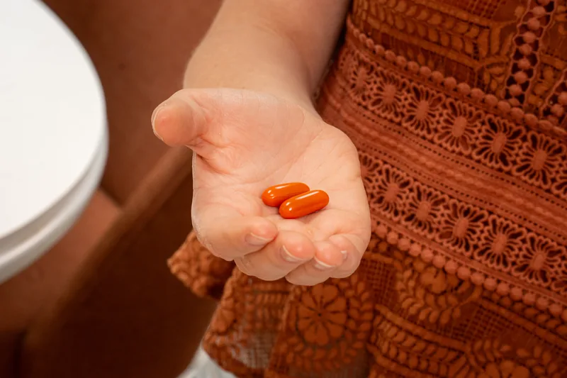 A palm holding small orange supplements, warm rust fabric behind.