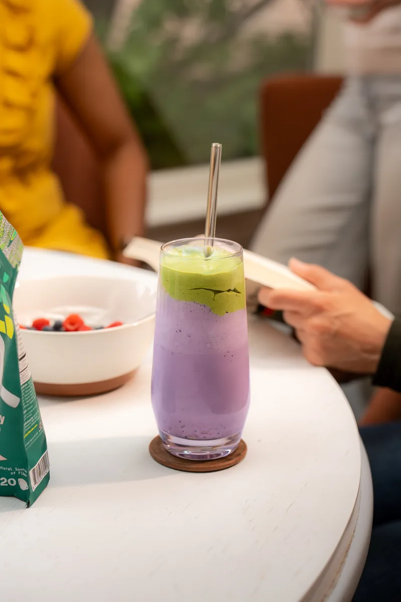 A tall violet smoothie topped with berries, backlit on a marble counter.