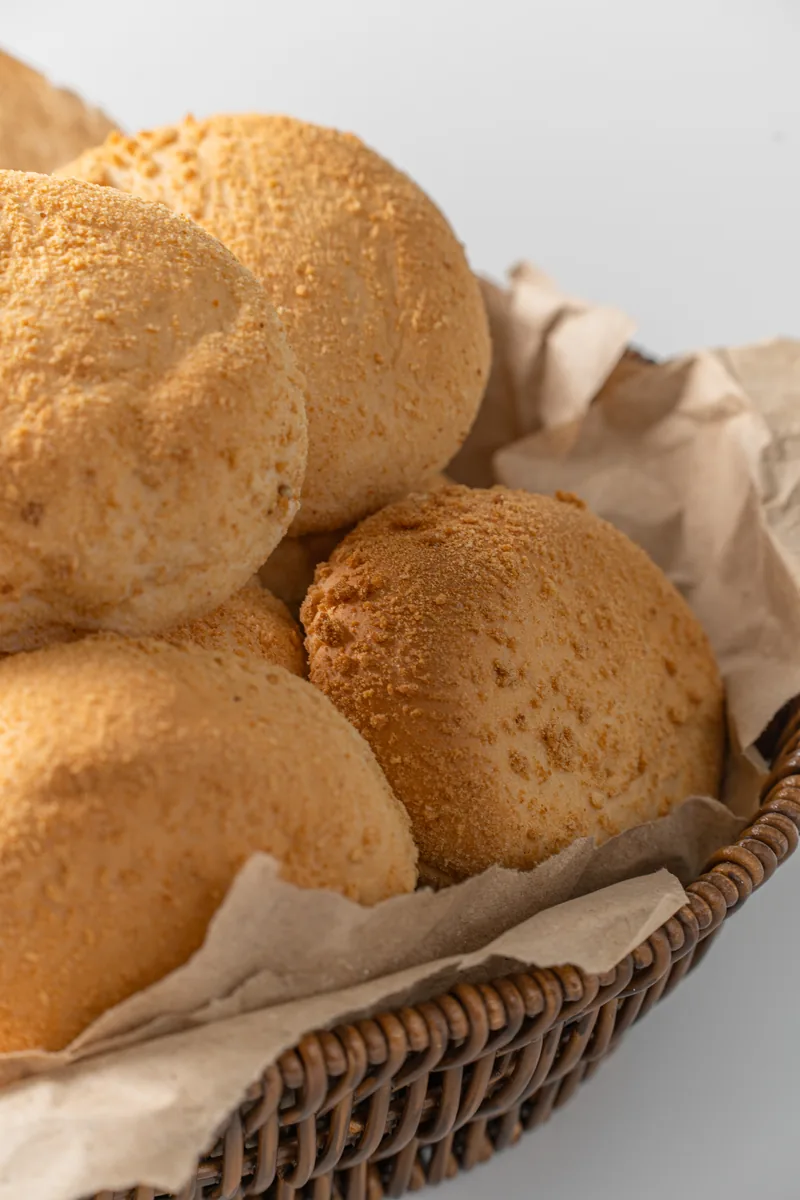 A paper lined basket piled with pandesal, more loaves soft behind.