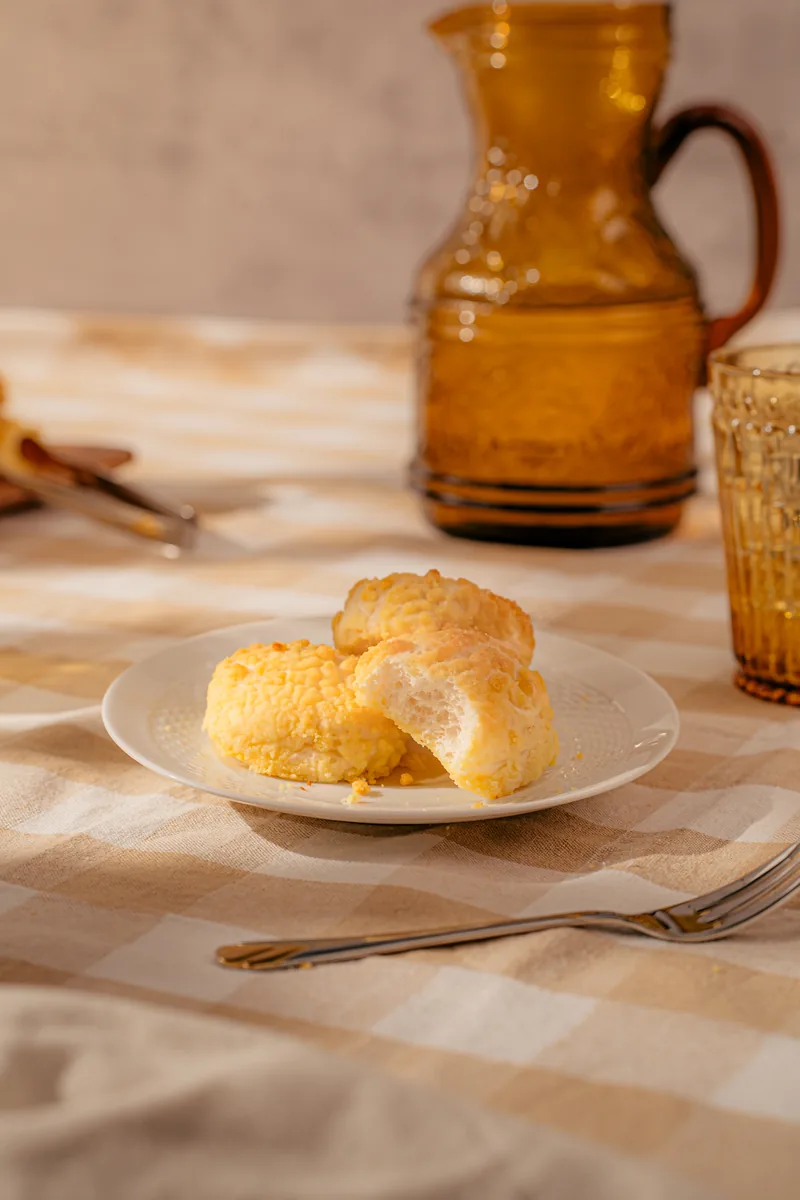 Cheese bread on a white plate on a gingham cloth, an amber glass jug behind.