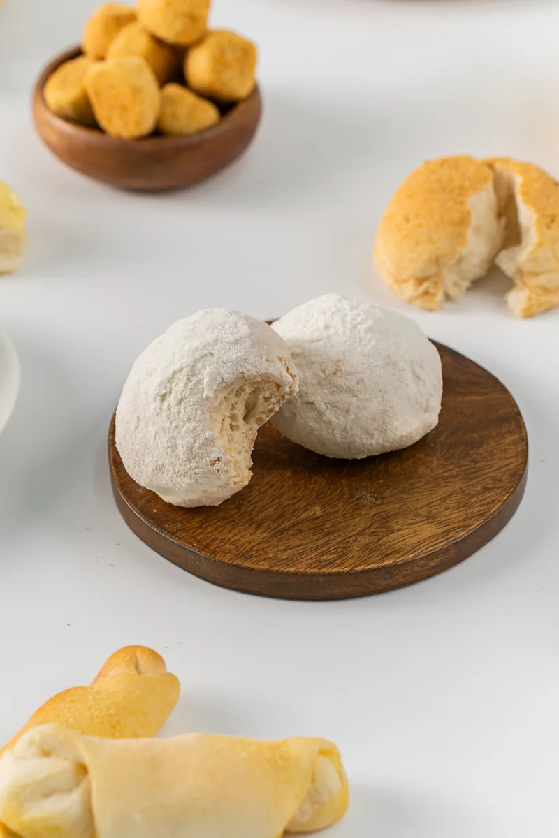 A sugar dusted bun broken open on a small wooden stand, more bread soft behind.