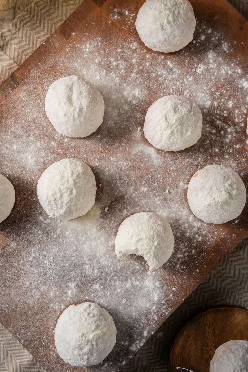 Sugar dusted milky donuts on a dark board under a scatter of flour.