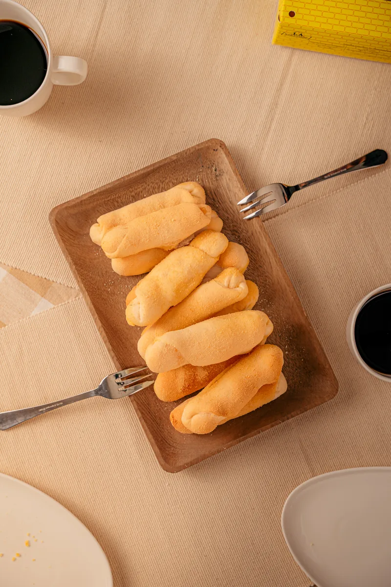 Spanish bread stacked on a wooden tray with a fork and a cup of coffee alongside.