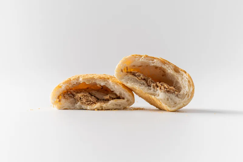 A tuna bun halved to show the filling, crumbs on white.
