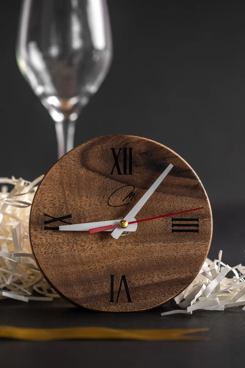 A round walnut desk clock leaning against a wine glass stem.