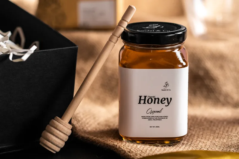 A honey jar with a wooden dipper leaning on the box edge.