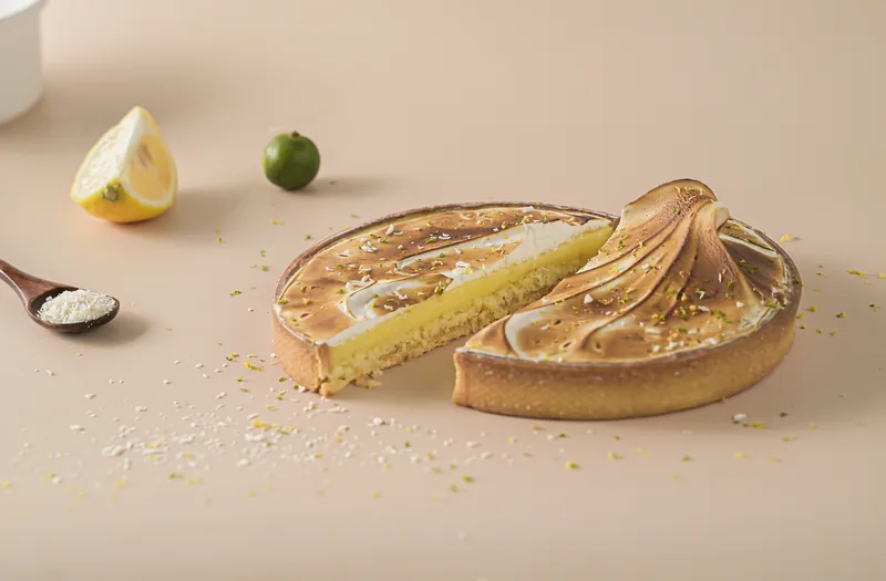 A calamansi meringue tart with a wedge cut away, a lemon slice and a whole calamansi behind.
