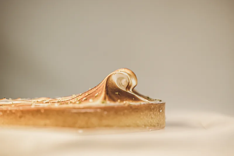 A calamansi meringue tart shot from the side, the torched meringue curling to a point.