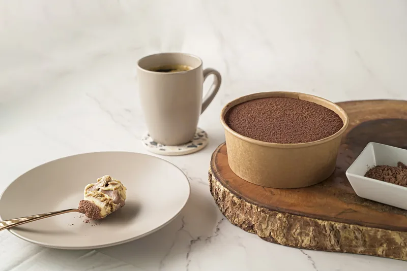 A spoonful of chocolate cup dessert set on a plate, the tub and a coffee behind it.