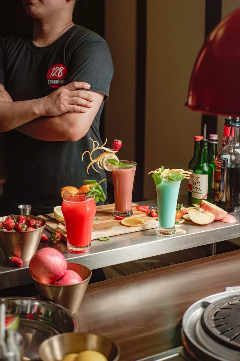 A staff member with crossed arms behind a line of finished drinks.