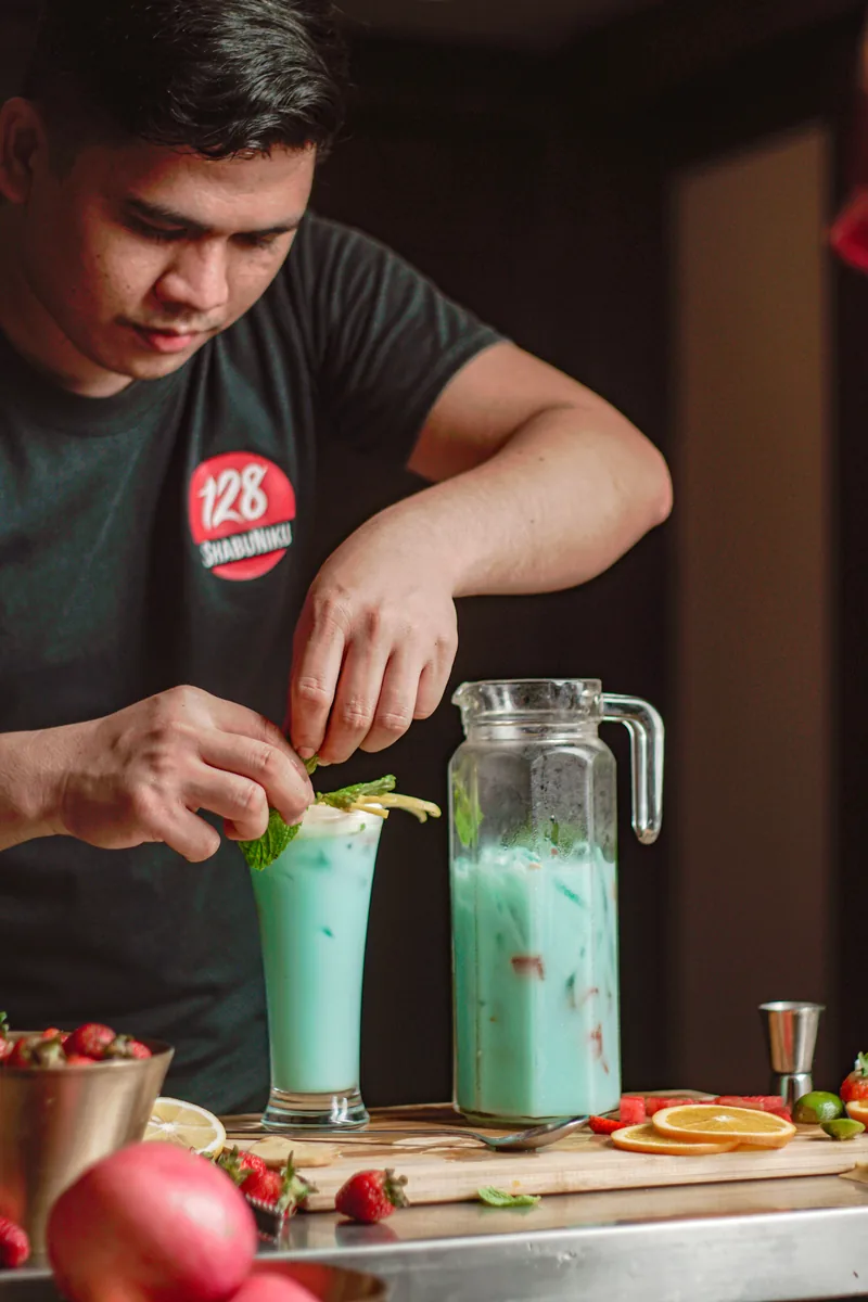 A staff member garnishing tall blue drinks at a steel counter.