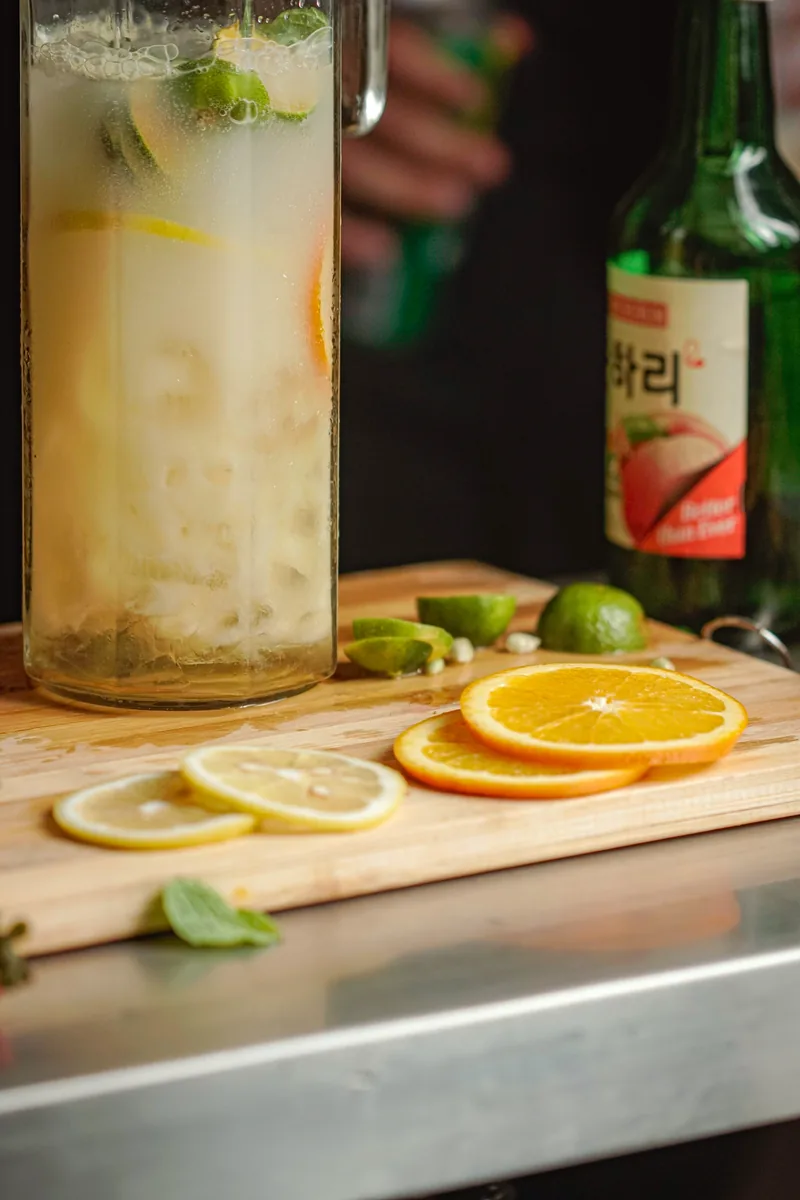 A citrus cooler and a soju bottle over a board of sliced lemons and limes.