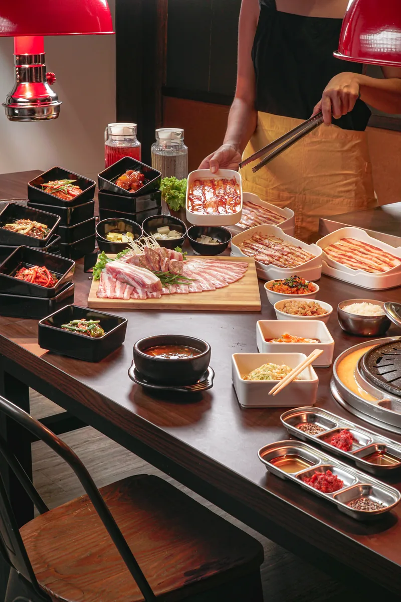 A shabu shabu spread across a dark table, staff reaching in under red lamps.