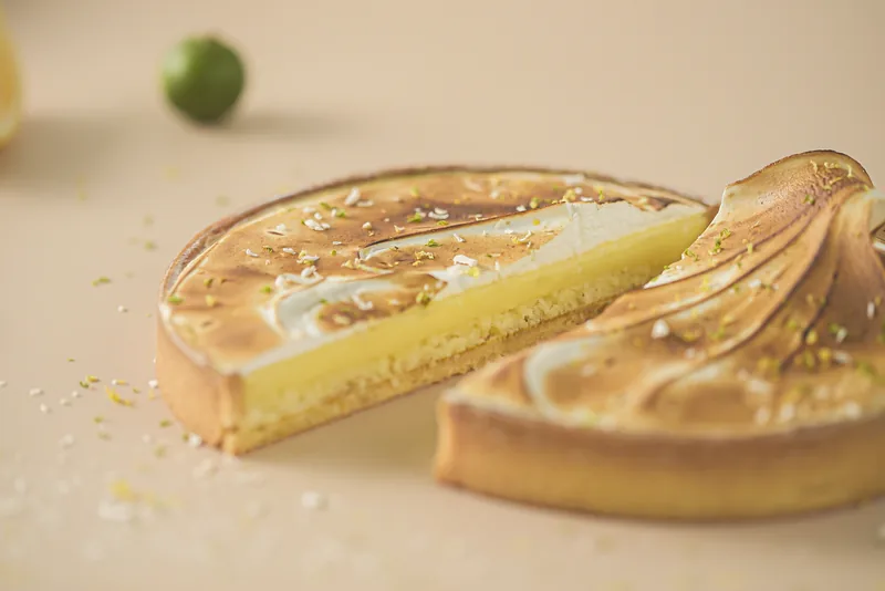 A calamansi meringue tart with one slice pulled away, zest scattered on the board.